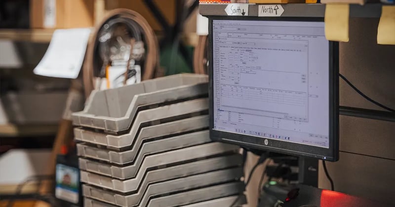 parts bins stacked next to a computer displaying EBMS, an ERP used for managing inventory